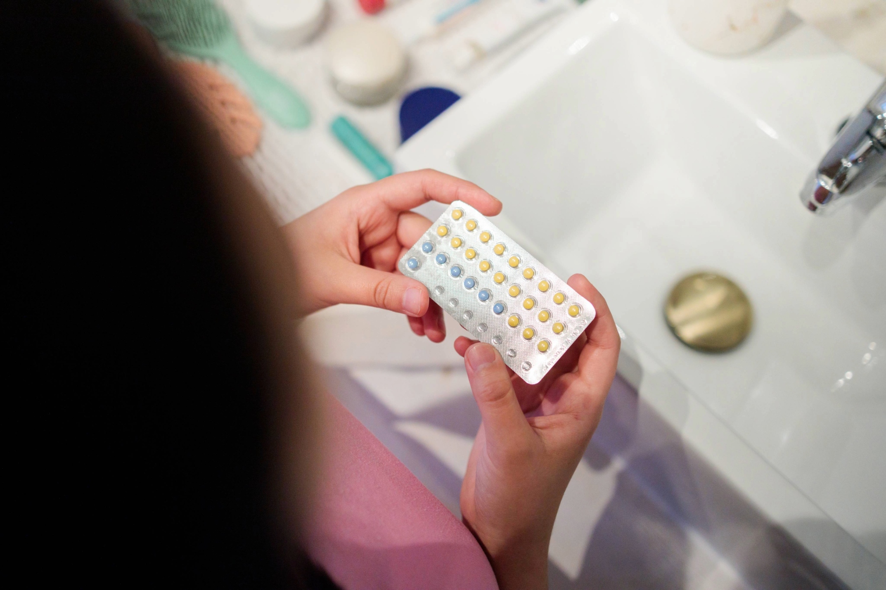 A woman holds a pack of birth control pills over the sink.