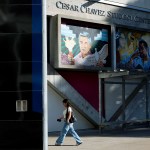 A person walks past a building with a sign reading “Cesar Chavez Student Center,” with painted murals of Cesar Chavez and Malcolm X on the wall above.