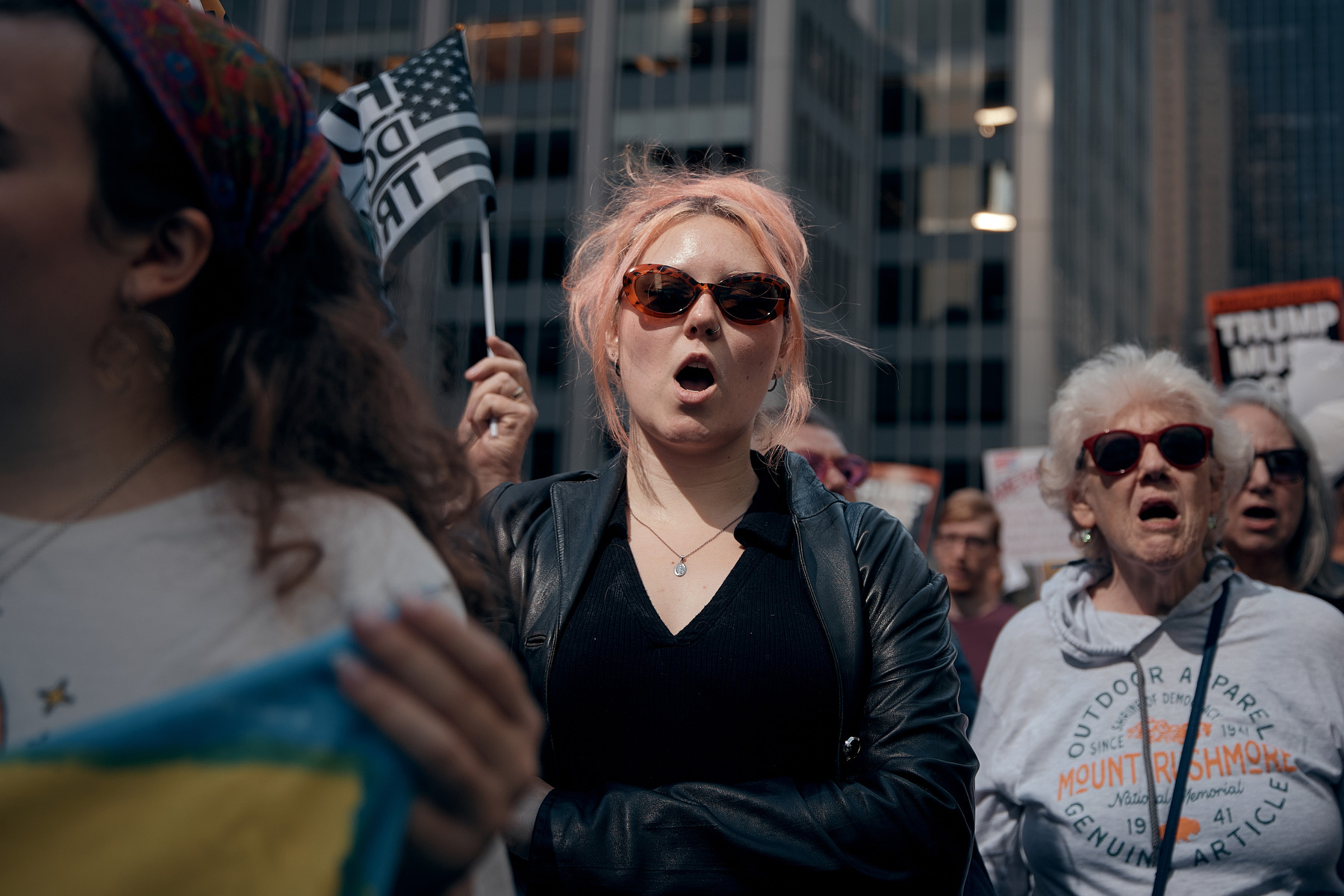 A young woman with pink hair chants during a protest, surrounded by other women.