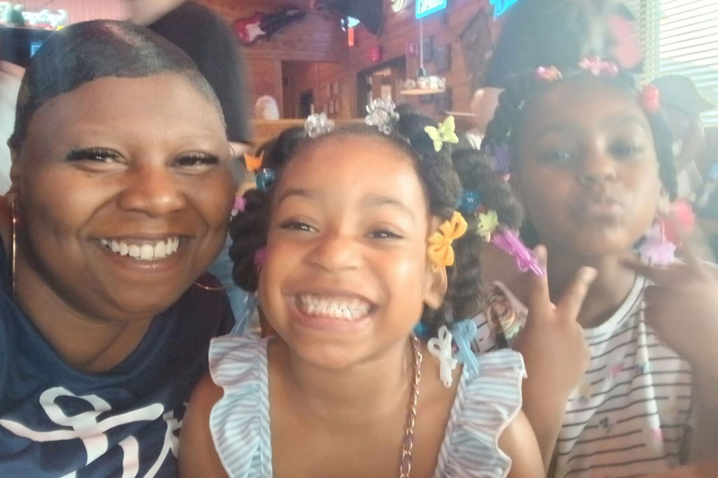 A woman smiles in a restaurant while posing with two young girls, all close together and facing the camera.