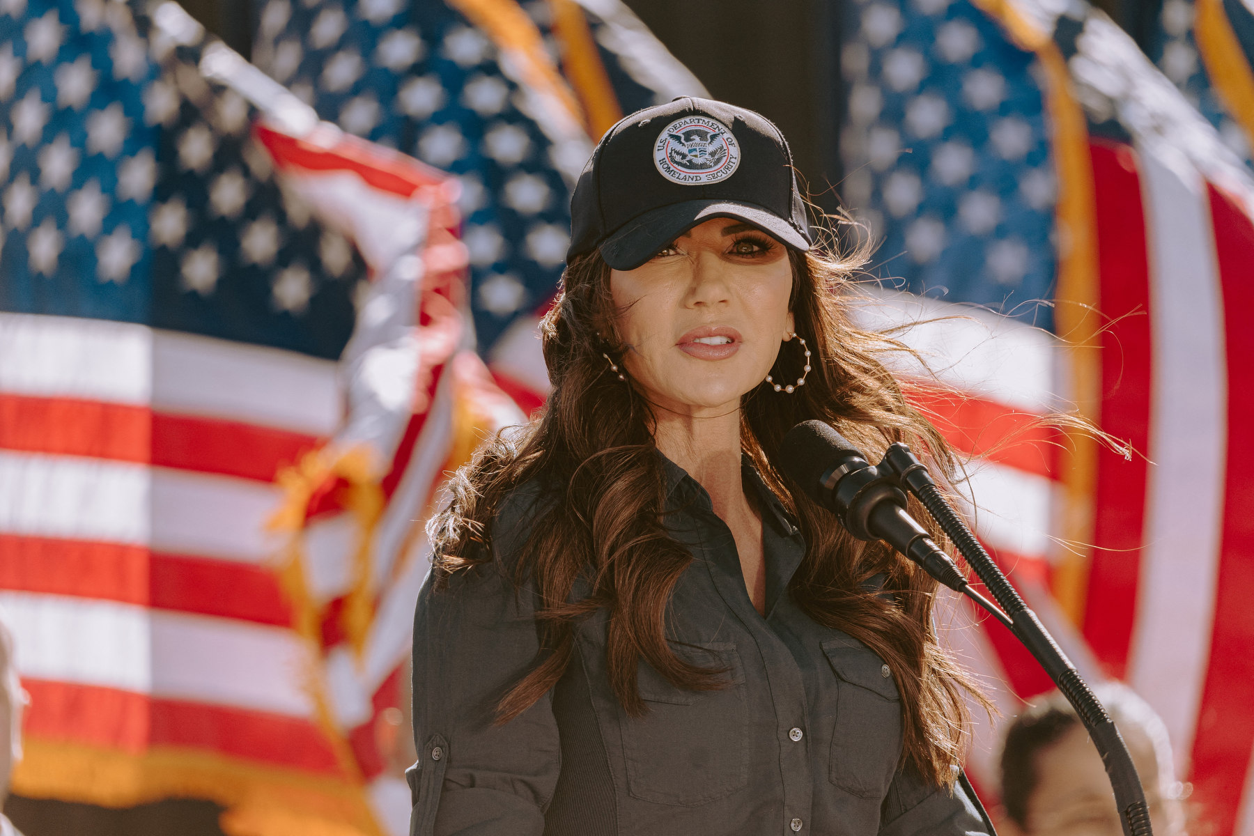 Noem stands in front of several American flags in militaristic attire.
