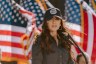 Noem stands in front of several American flags in militaristic attire.