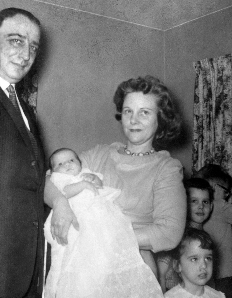 Black and white portrait of Viola Liuzzo holding a baby while standing beside a man, with three young children nearby in a home setting.