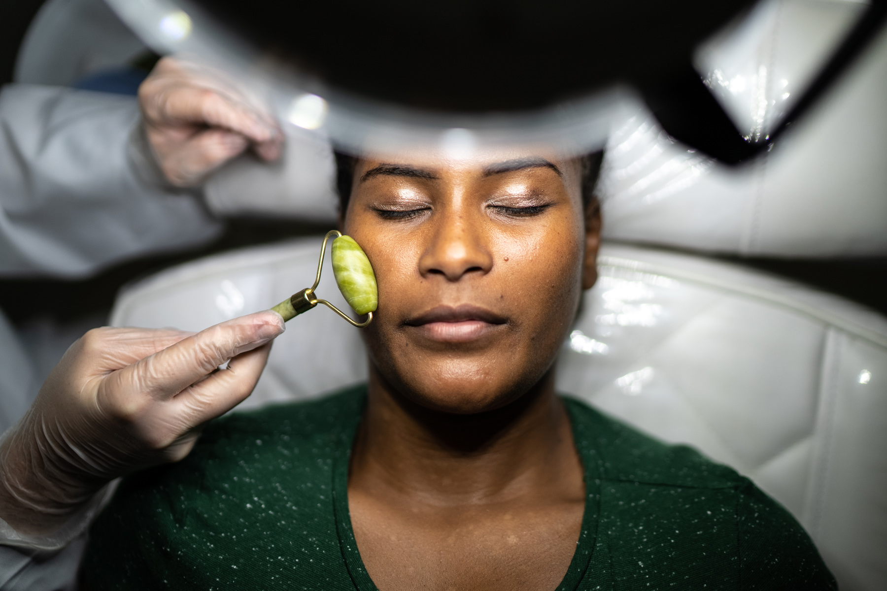 A woman receives a facial massage with a crystal roller under a light.