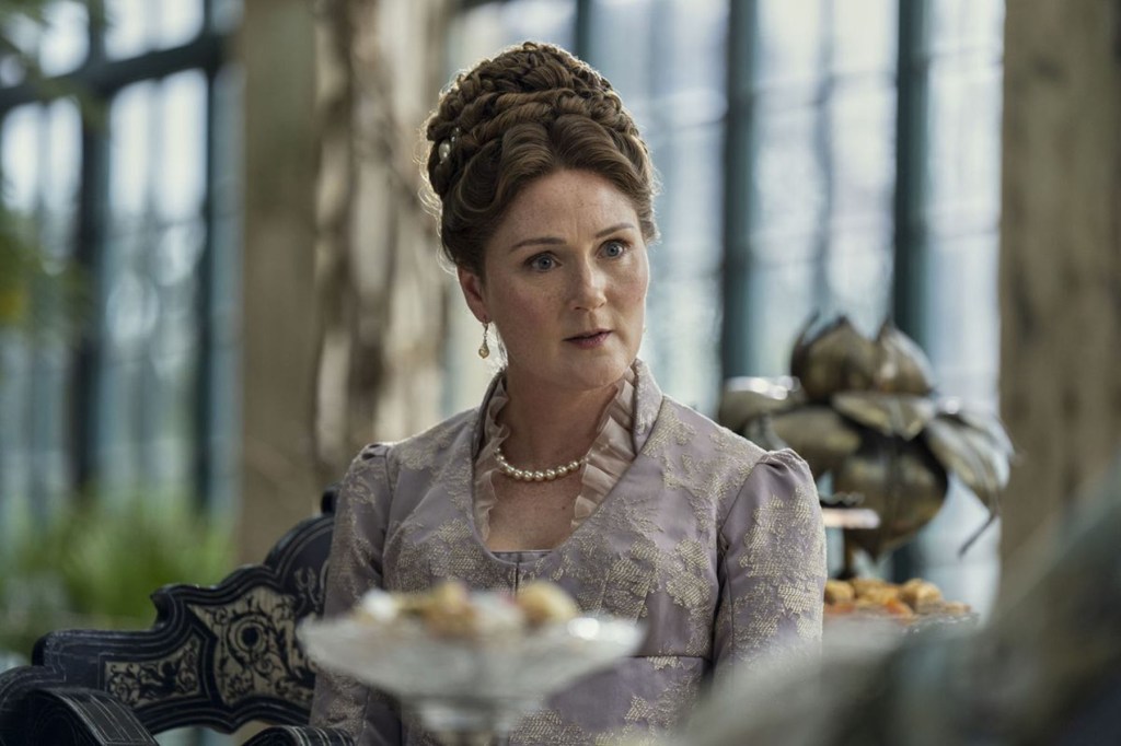 Ruth Gemmell as Violet Bridgerton sits at a table in a Regency-era dress with her hair styled up, looking surprised during a conversation.