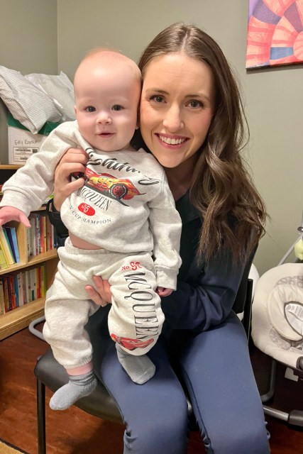 A mother holds a baby, smiling into the camera.