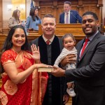 Nabilah Parkes takes the oath of office inside the Georgia Senate chamber, raising her right hand while holding a book, with her husband holding their baby beside her.