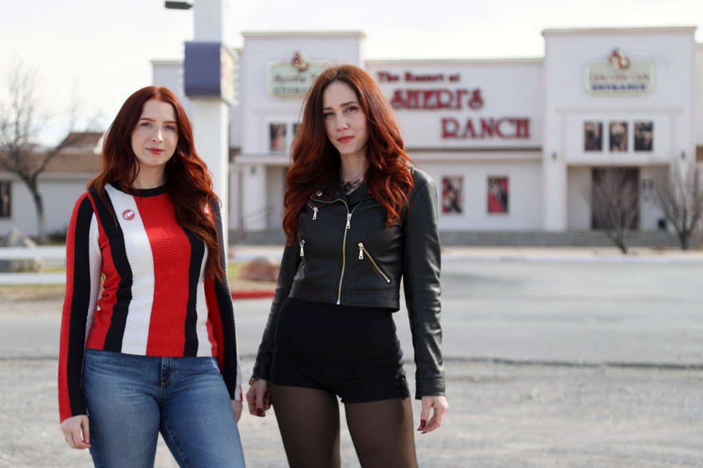Two women with red hair stand in front of a white building.