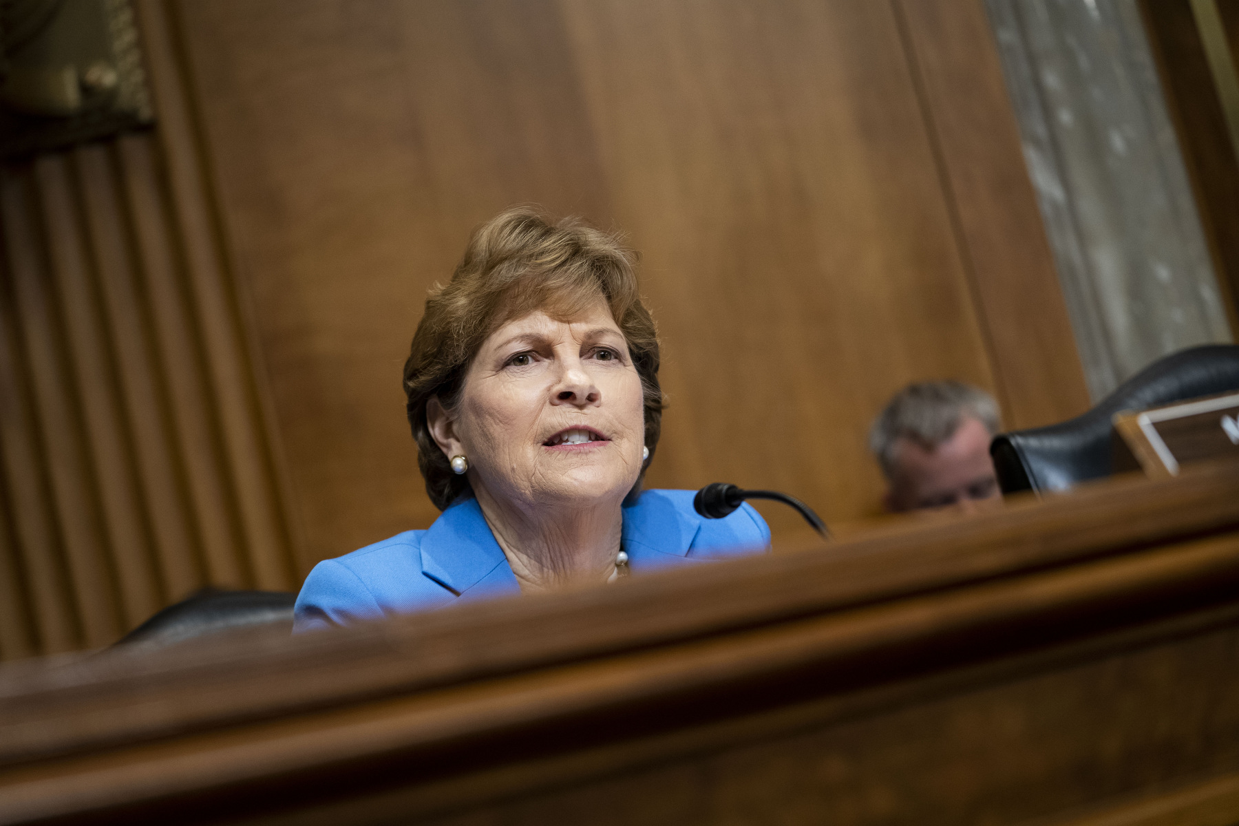 Shaheen seated at a desk in a blue suit.