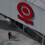 An aerial view shows a person pushing a shopping cart toward the entrance of a Target store beneath the company’s red logo.