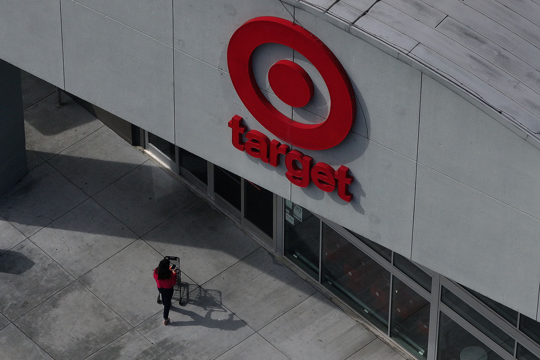 An aerial view shows a person pushing a shopping cart toward the entrance of a Target store beneath the company’s red logo.