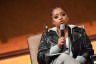 Tamika Mallory sits in a chair holding a microphone while speaking during a town hall event.