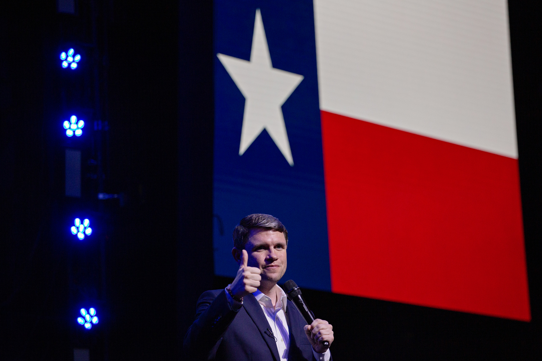 Talarico gives a thumbs up while standing in front of a giant Texas flag.