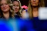 Several women are out of focus in the foreground while a red Make America Healthy Again hat can be seen in the background.