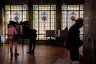 People vote at individual booths inside a dimly lit polling place, silhouetted against large stained-glass windows in the background.