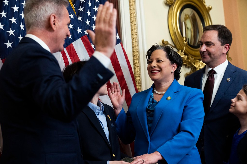 Rep. Jennifer McClellan raises her hand during a ceremonial swearing-in as family members stand beside her.