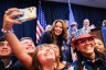A group of people flank a woman on stage with American flags in the background.