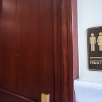 A bathroom door with a restroom sign showing a femme and masc figure alongside a person using a wheelchair.