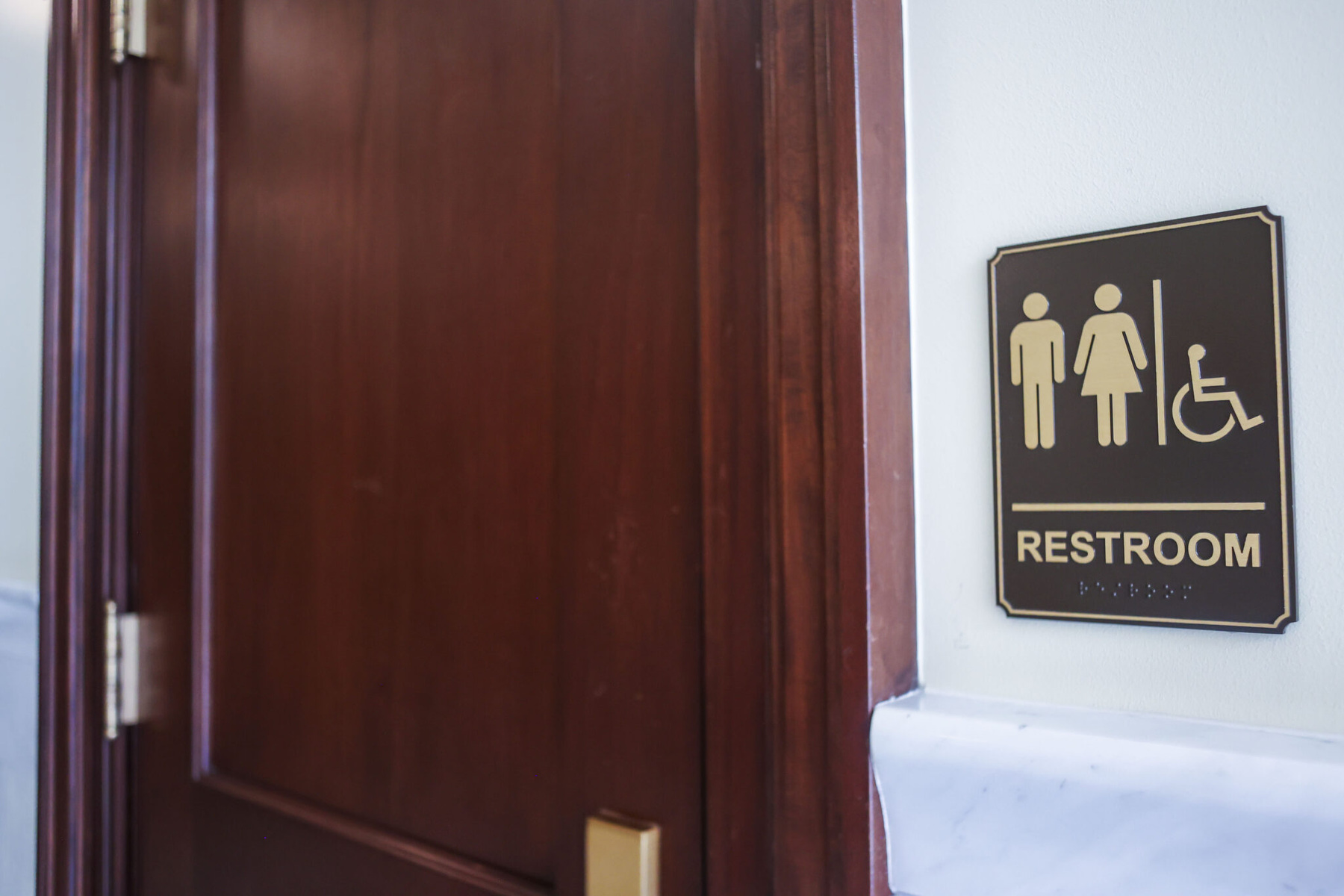 A bathroom door with a restroom sign showing a femme and masc figure alongside a person using a wheelchair.
