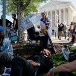 People gather outside the U.S. Supreme Court in Washington, D.C., with demonstrators resting in the shade and holding signs about birthright citizenship and the Constitution.