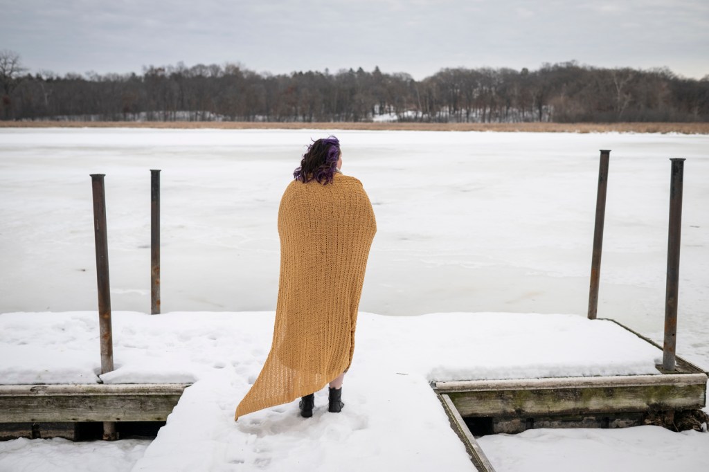 A woman wrapped in a yellow blanket looks out at a snowy waterway.