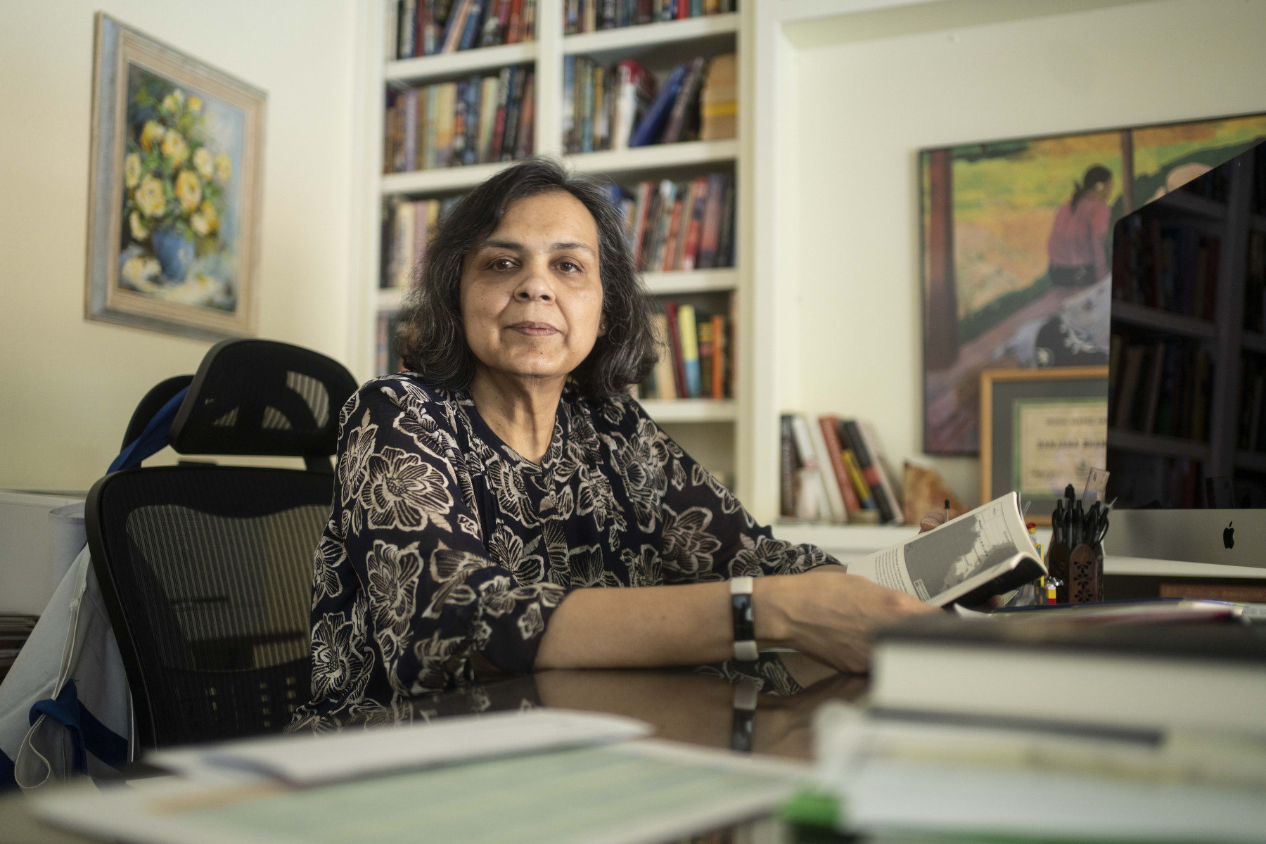 A woman sits at a desk in her home looking into the camera.