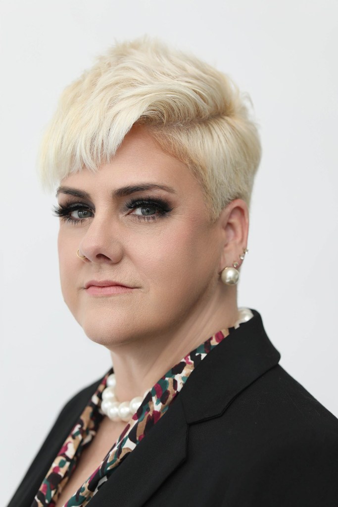 A woman with short blonde hair looks directly at the camera.