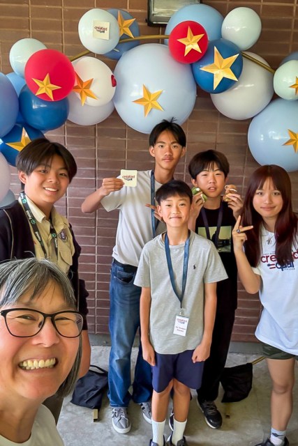 Students smile at the camera with their teacher with balloons and stars in the background.