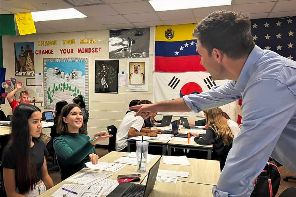 A teacher talks to a student in a history classroom.