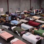 Rows of beds line up in a massive shelter for unhoused people.