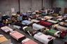 Rows of beds line up in a massive shelter for unhoused people.