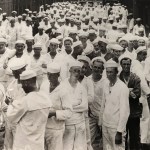 A large group of sailors in white uniforms and caps stand closely together outdoors, filling the frame as they face the camera.