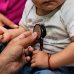A doctor holds a stethoscope up to a baby's heart.