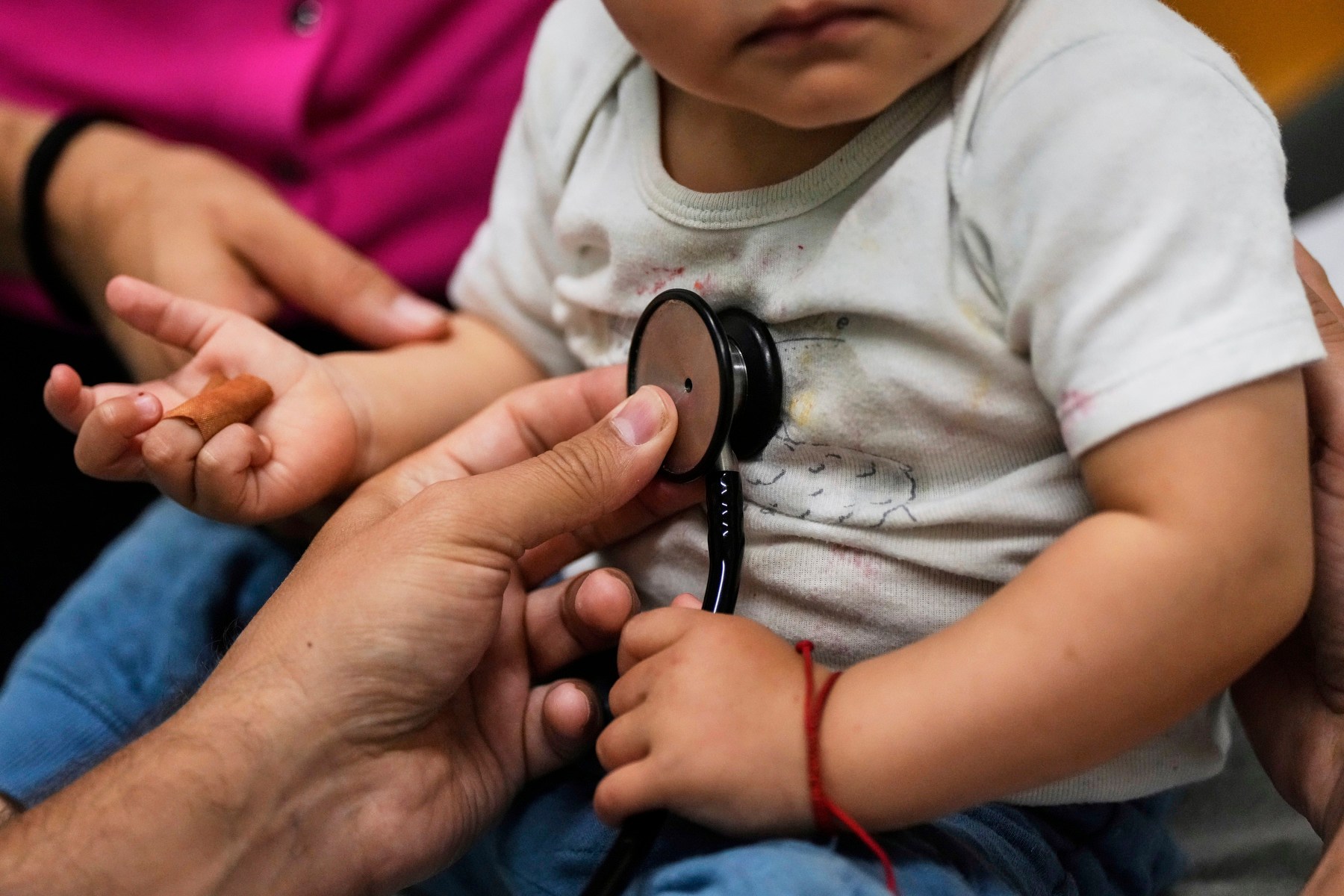 A doctor holds a stethoscope up to a baby's heart.