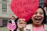 A domestic worker holds a large red paper heart during a City Hall advocacy action in New York City while Allison Julien stands in the background with a pink paper heart.