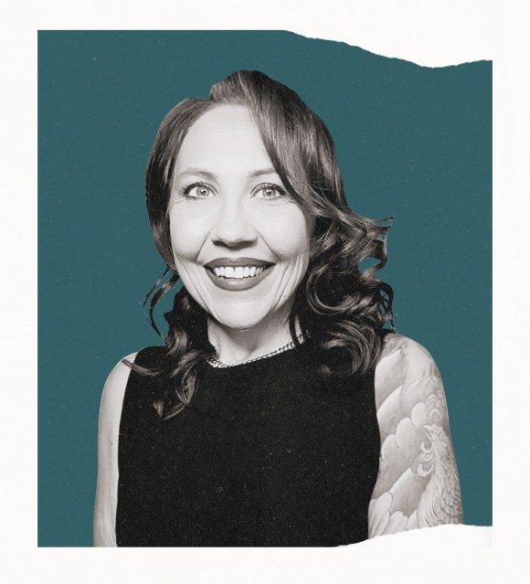 portrait of a smiling woman speaking at a microphone against a light teal background.