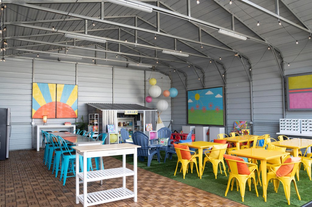 A colorful indoor common area includes tables, chairs, murals, paper lanterns and a small children’s library.