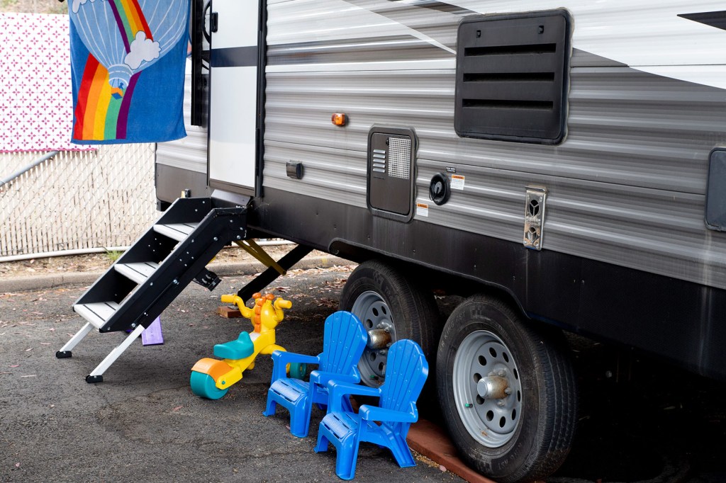 Small plastic children’s chairs and a toy sit outside a travel trailer near its steps.