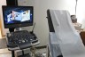 An ultrasound machine sits beside an exam table covered with white exam paper in a medical clinic room.