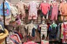 Baby clothes in a range of sizes hang on racks and wall hooks inside a donation room.