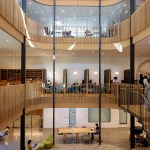 Interior view of Smith College showing a wood paneled academic building with glass walls, study tables, bookshelves and students working throughout the open space.