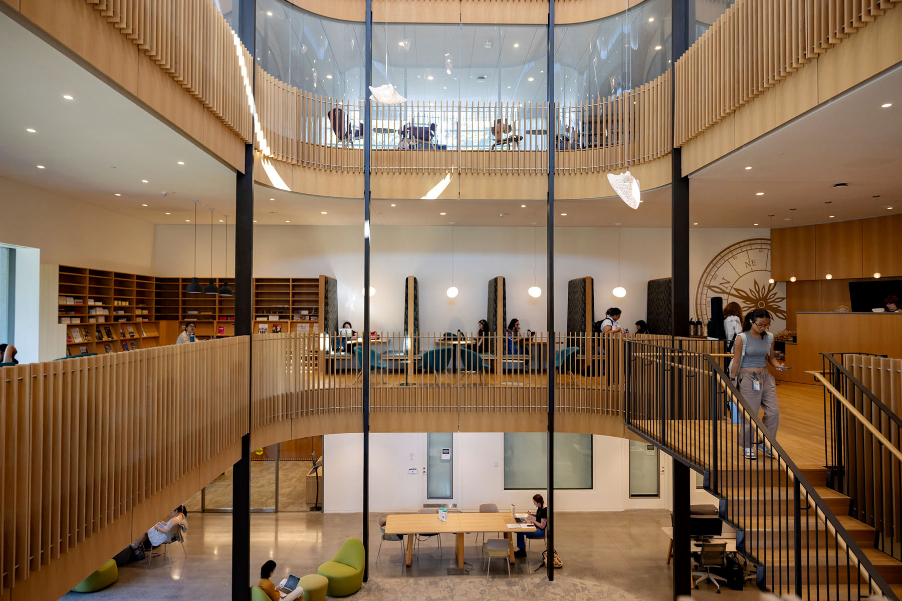 Interior view of Smith College showing a wood paneled academic building with glass walls, study tables, bookshelves and students working throughout the open space.