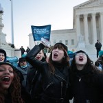 Protesters chant outside the U.S. Supreme Court, holding boxes labeled “abortion pills” and signs that read “abortion is essential.”