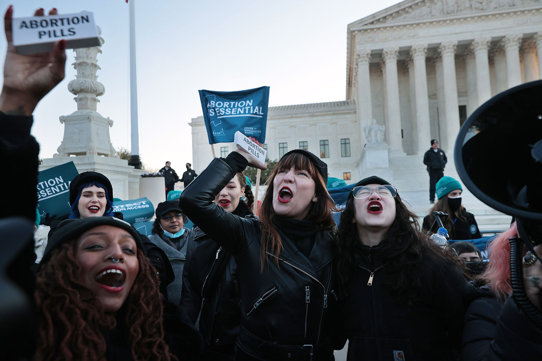 Protesters chant outside the U.S. Supreme Court, holding boxes labeled “abortion pills” and signs that read “abortion is essential.”