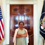 A woman stands in between two flags with her arms crossed.