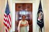 A woman stands in between two flags with her arms crossed.