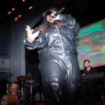 BL Shirelle performing onstage with a microphone in their hand flanked by two band members.