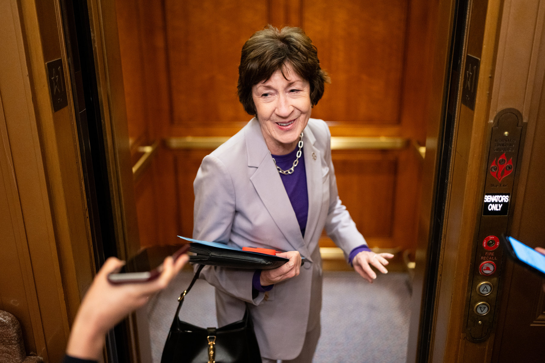 A woman smiles at reporters trying to interview her while she steps into an elevator.
