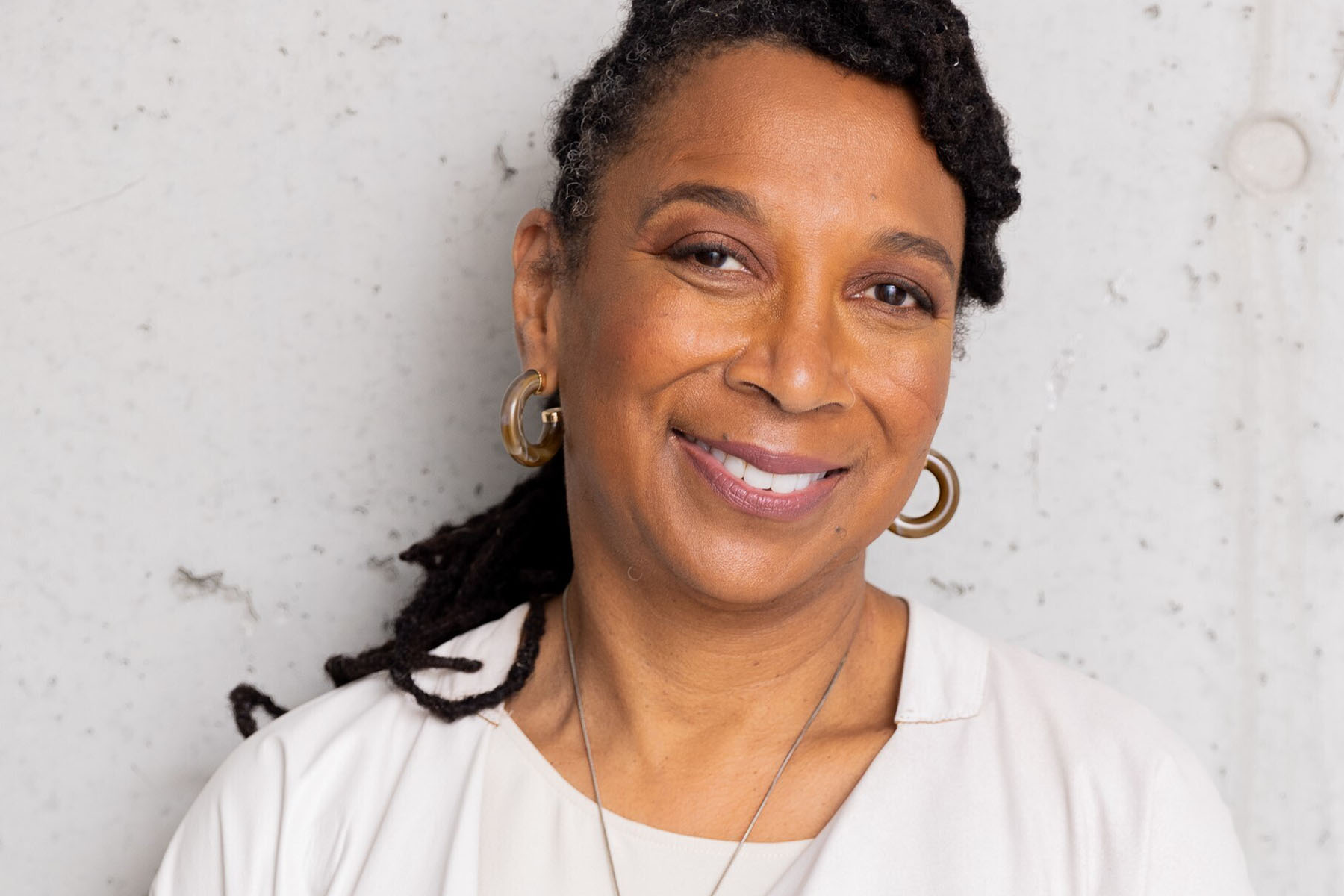 Kimberlé Crenshaw smiles at the camera while standing against a wall.