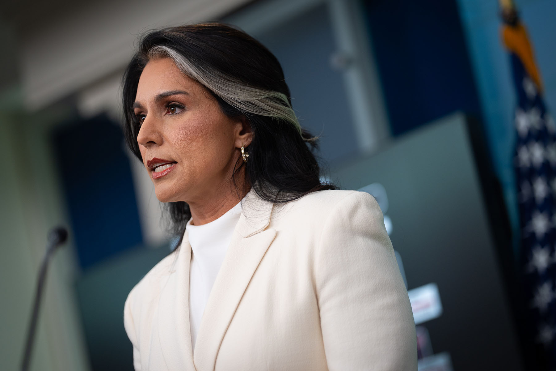 Tulsi Gabbard, in a white blazer speaks at a podium at the White House briefing room.